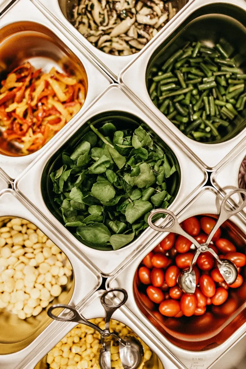 Tabuleiros de buffet com espinafres, feijão-verde, grão e tomate-cereja