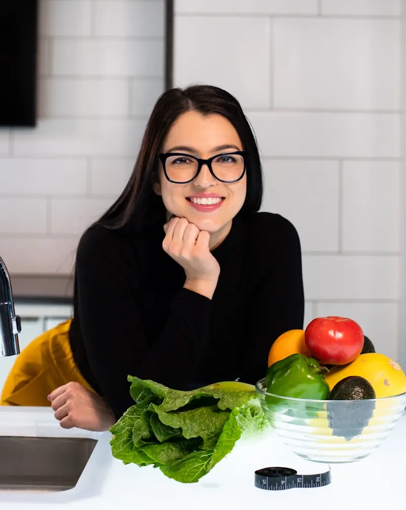 Nutricionista a sorrir numa cozinha, com legumes frescos à sua frente